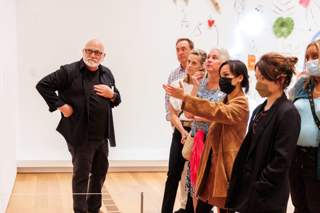 A man in all black talks to a group of smartly dressed adults inside the modern and contemporary galleries at the High Museum